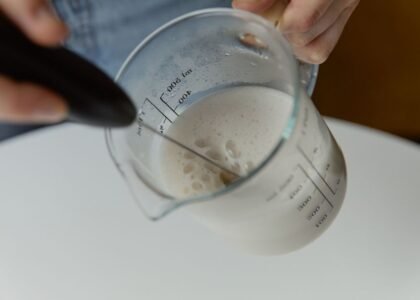 A person frothing milk in a measuring cup with a manual milk frother.