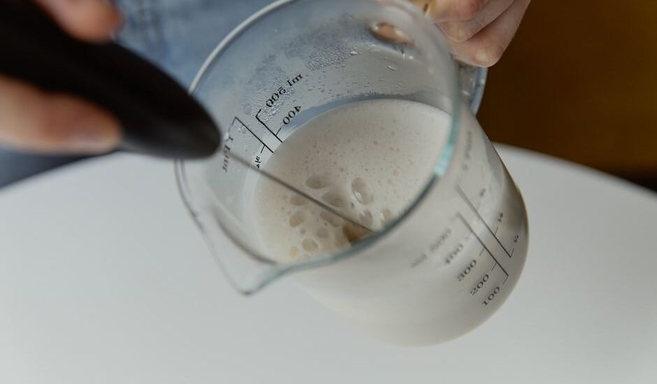 A person frothing milk in a measuring cup with a manual milk frother.