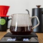 A pour-over stand with scale, coffee brewing equipment, and a glass carafe filled with brewed coffee.