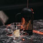 A French press and a glass cup on a table, illustrating siphon coffee maker vs French press.