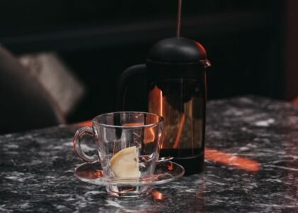 A French press and a glass cup on a table, illustrating siphon coffee maker vs French press.