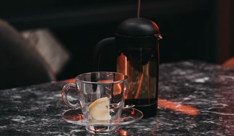 A French press and a glass cup on a table, illustrating siphon coffee maker vs French press.