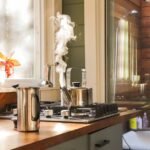 A stovetop kettle steaming on a gas stove next to a French press, illustrating the stovetop vs electric kettle debate.