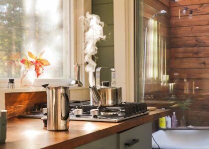 A stovetop kettle steaming on a gas stove next to a French press, illustrating the stovetop vs electric kettle debate.