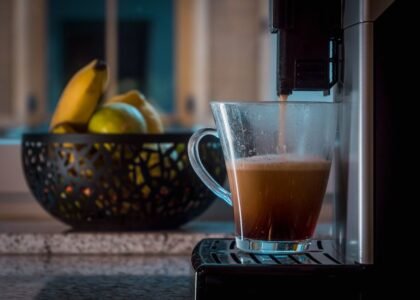 A single serve drip coffee maker pouring coffee into a clear mug, with fruit in the background, illustrating home brewing.