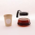 A coffee carafe filled with brewed coffee next to a paper cup, illustrating deep cleaning methods.