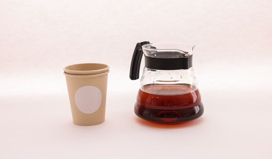 A coffee carafe filled with brewed coffee next to a paper cup, illustrating deep cleaning methods.