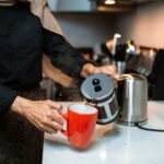 A person pours coffee from a French press into a red mug, illustrating the cleaning process.