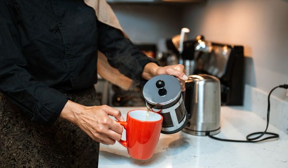 A person pours coffee from a French press into a red mug, illustrating the cleaning process.