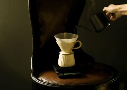 A hand pours hot water from a kettle into a ceramic pour-over coffee maker.
