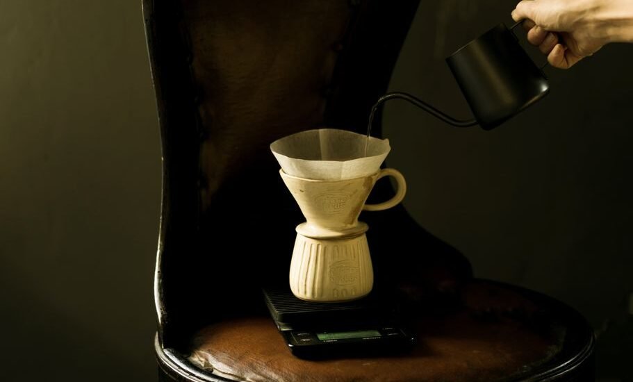 A hand pours hot water from a kettle into a ceramic pour-over coffee maker.
