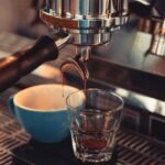 A close-up of espresso being extracted into a glass and cup, illustrating single vs double filter espresso.