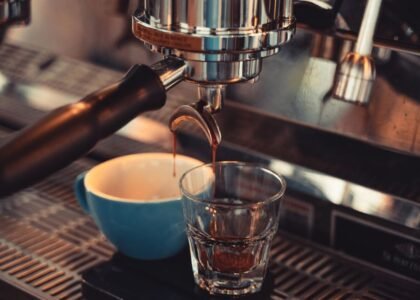 A close-up of espresso being extracted into a glass and cup, illustrating single vs double filter espresso.