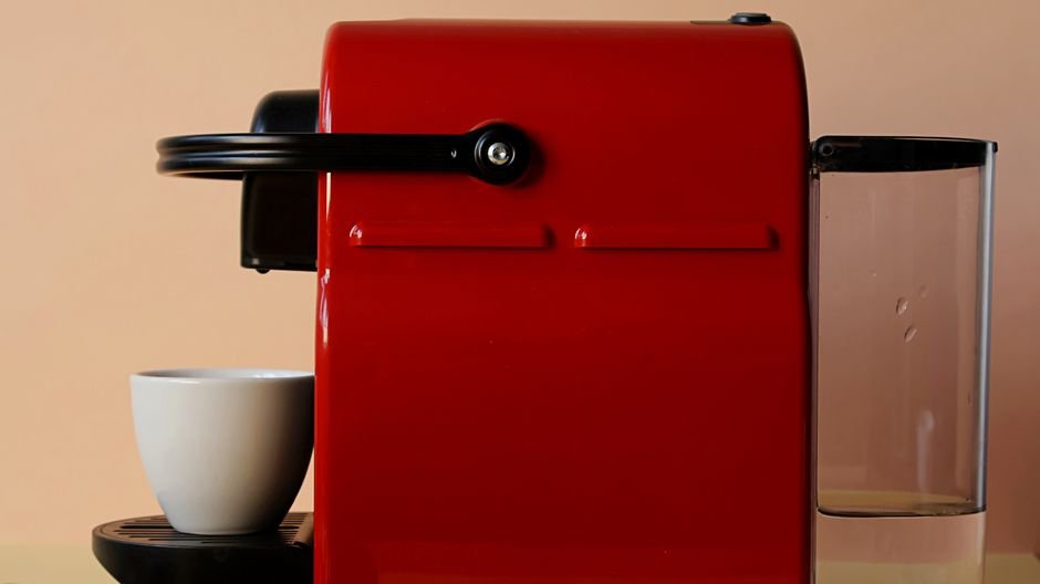 A red single-serve pod coffee maker next to a white cup, relevant to coffee maker reviews.