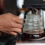 A hand pours coffee from a thermal carafe coffee maker, illustrating the brewing process.