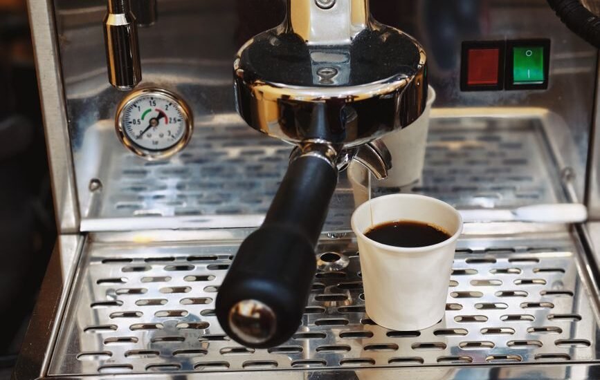 A close-up of an espresso machine showing a pressure gauge and a cup of brewed coffee, relating to ideal espresso pressure.
